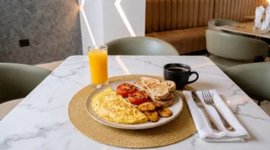Plated breakfast of omelette, plantain, grilled tomato and toast with orange juice and coffee