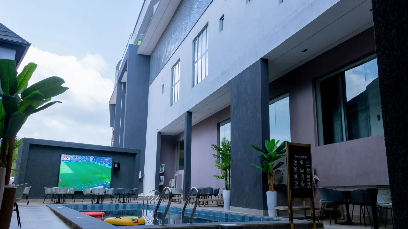 Courtyard pool with lounge seating and a large outdoor screen showing football