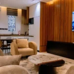 Apartment living room with sofas, wood-panelled TV wall and an open kitchen