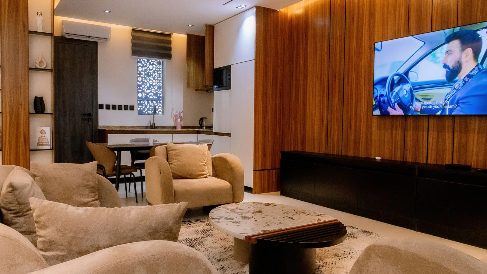 Apartment living room with sofas, wood-panelled TV wall and an open kitchen