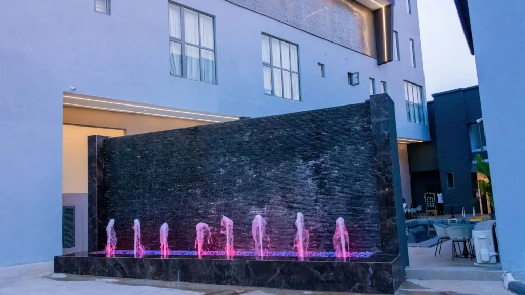 Stone water wall with pink-lit fountain jets at dusk
